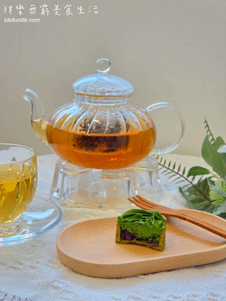 木盤上放著切半的紅豆抹茶生巧克力玫瑰塔,切面可見上層濃綠色抹茶內餡、底層顆粒狀紅豆餡與酥脆塔皮,後方搭配玻璃茶壺與茶杯。
